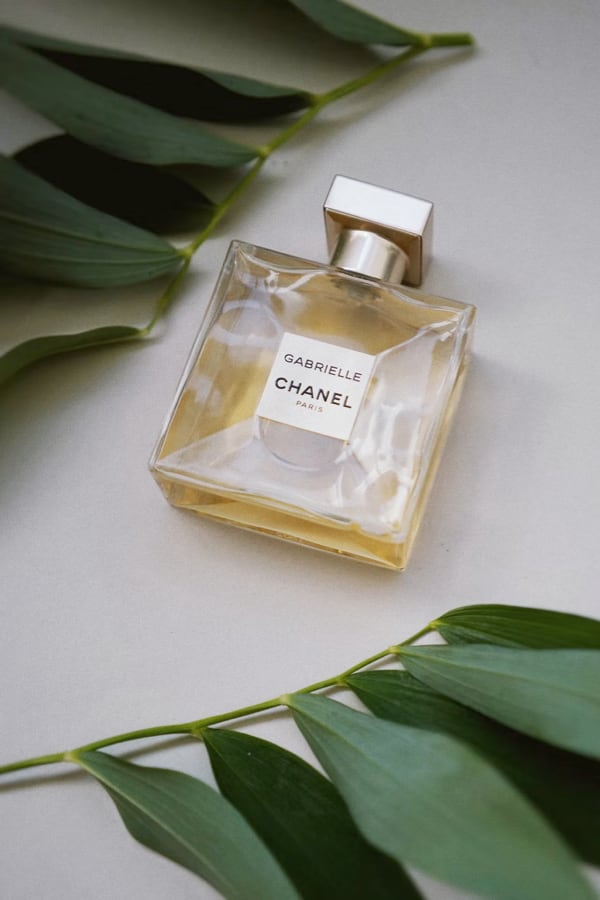 Bottle of Gabrielle Essence Eau De Parfum on a table with green leaves around it.